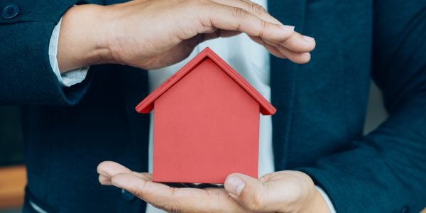 Business man hand hold the house model  saving small house. House insurance